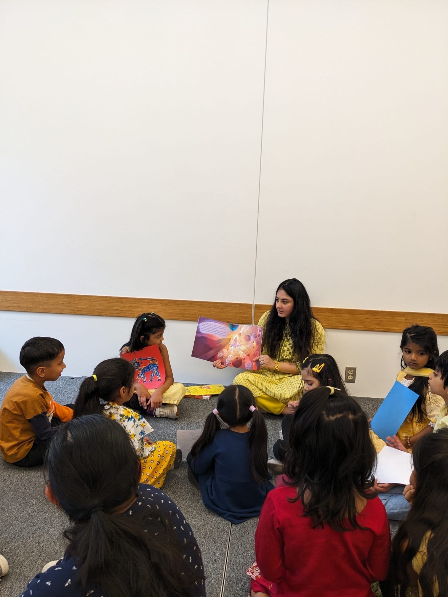 Divvya Singh reading aloud to children seated in a circle at the Urbana-Champaign public library